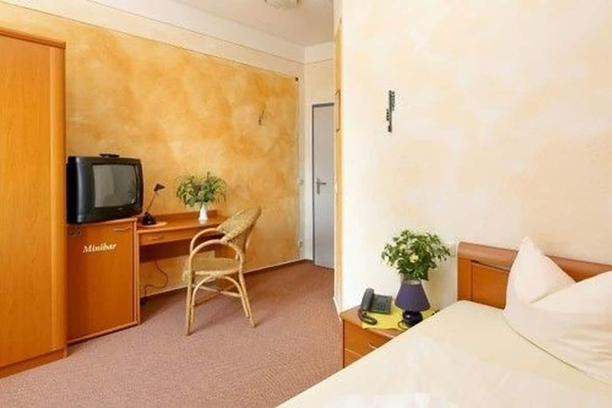 Een hotelkamer met een bed, een bureau met een televisie, een stoel en een potplant.