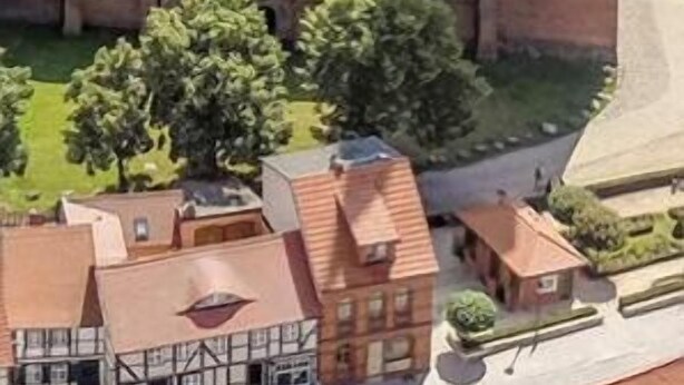 Un modelo de un edificio histórico con una gran torre central y ventanas arqueadas, rodeado de edificios y árboles más pequeños.