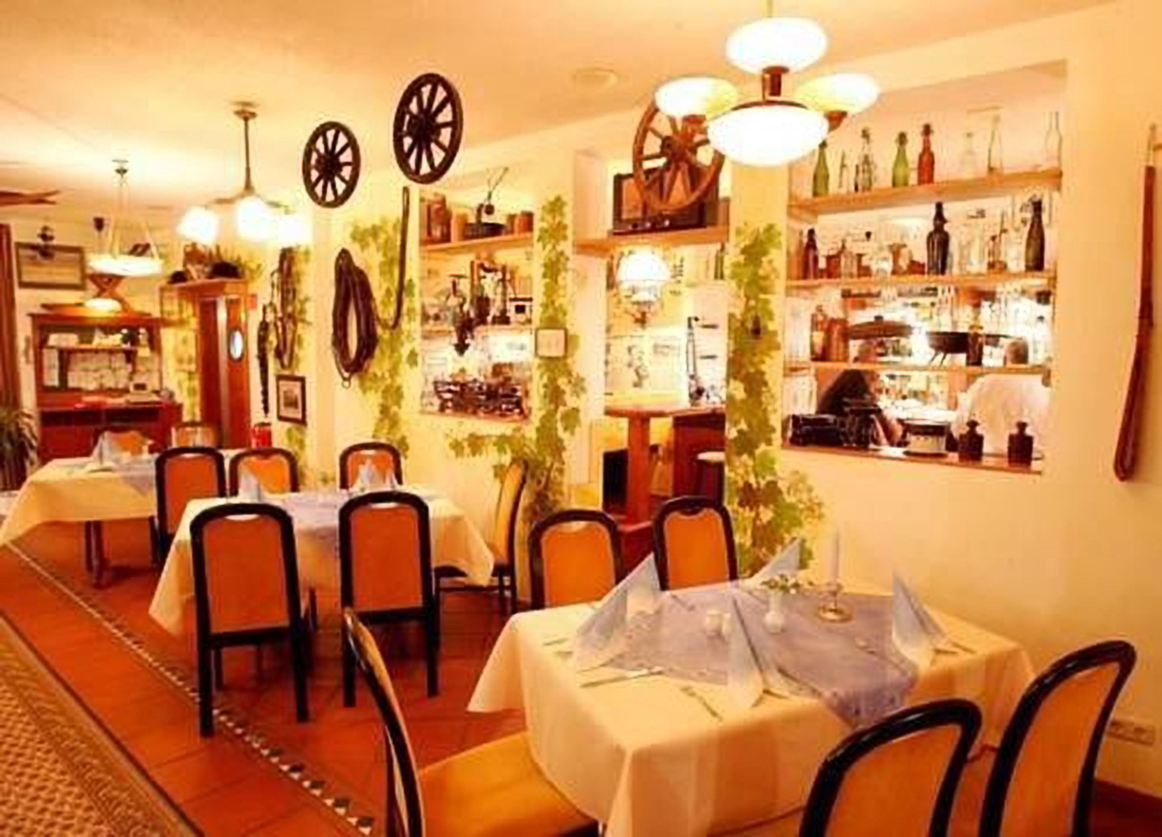 A restaurant with multiple tables and chairs, decorated with hanging lights and wall-mounted decorations.