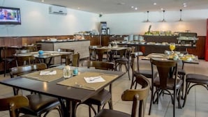 En restaurant med flere borde og stole, en disk med drikkeautomat og et fjernsyn ophængt på væggen.