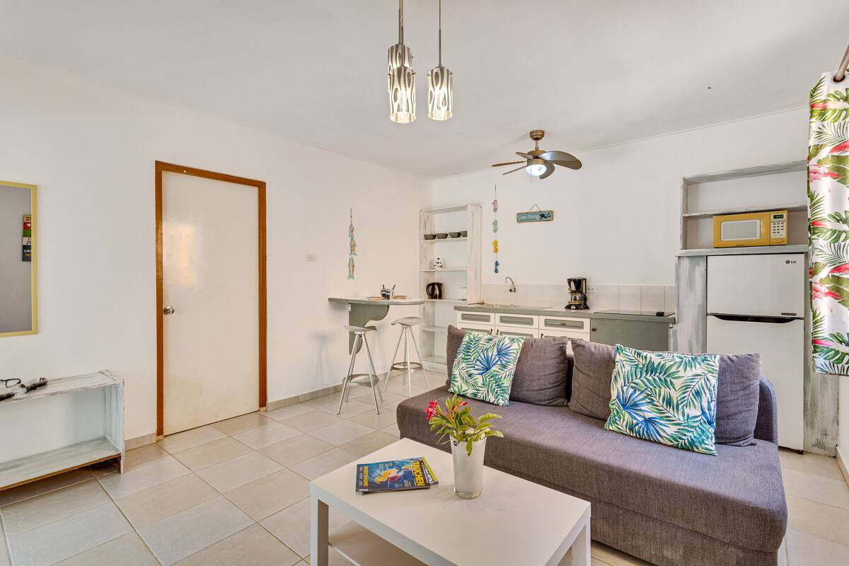 A modern living room with a sofa, a coffee table, and a kitchen area in the background.