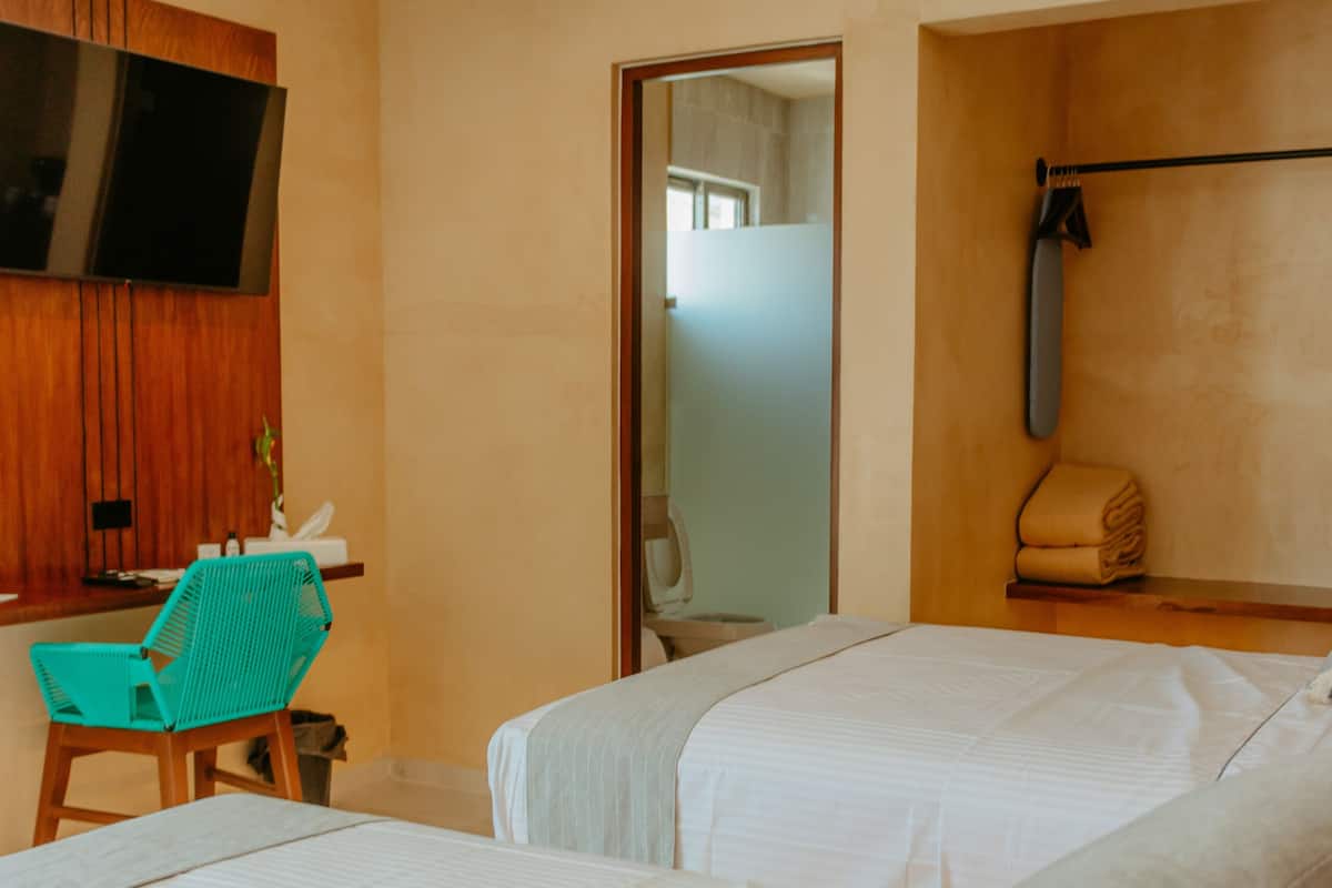 Habitación de hotel con dos camas, ventilador de techo, televisor, escritorio y una silla.