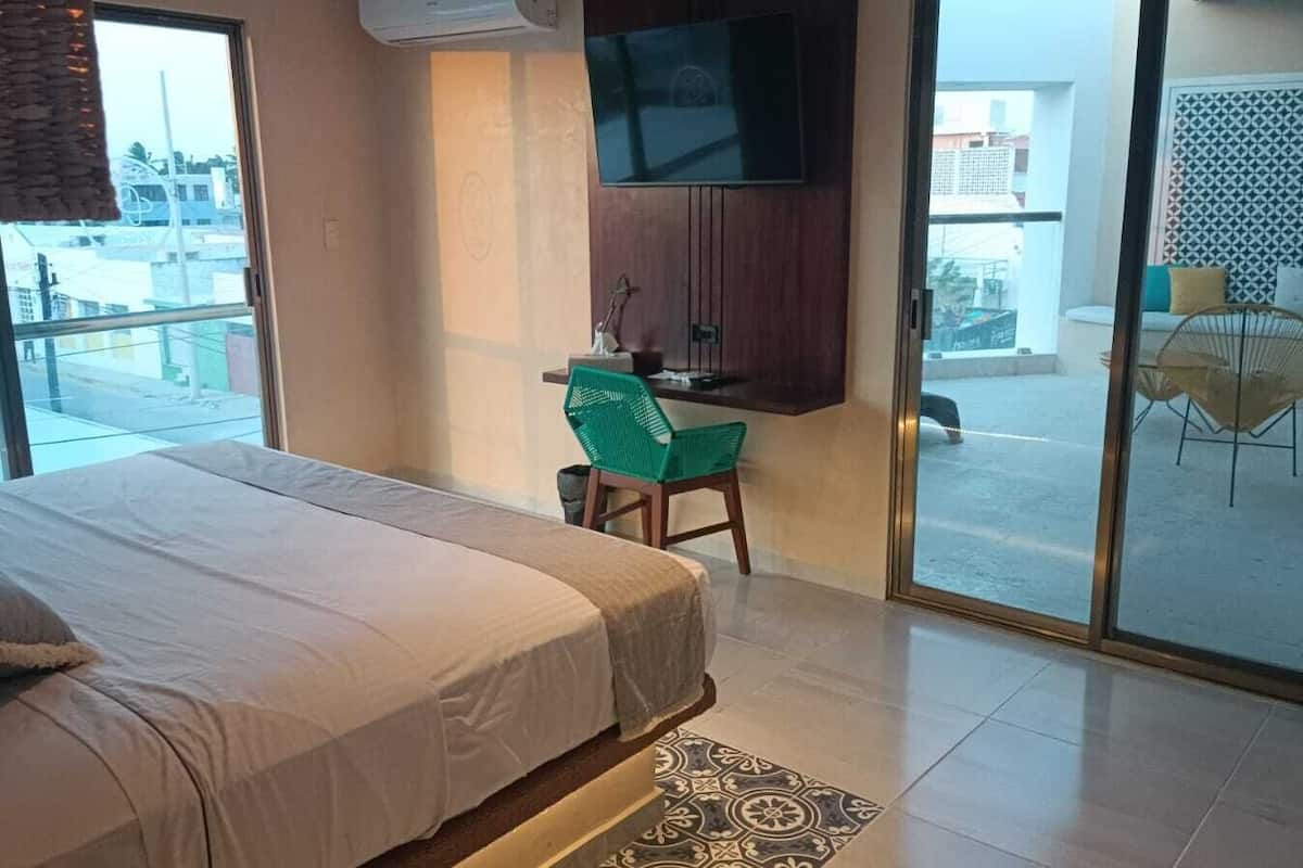 Habitación de hotel con cama, escritorio, silla, televisor y vistas al exterior.