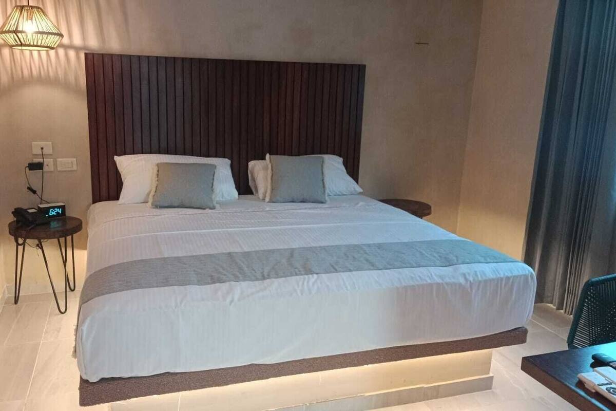 Una habitación de hotel moderna con una cama grande, una mesita de noche con un reloj y una pequeña mesa con una silla.