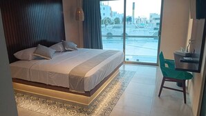 A modern bedroom with a large bed, a green chair, and a view of the city through a large window. - Hotel Yaxactun (Progreso)