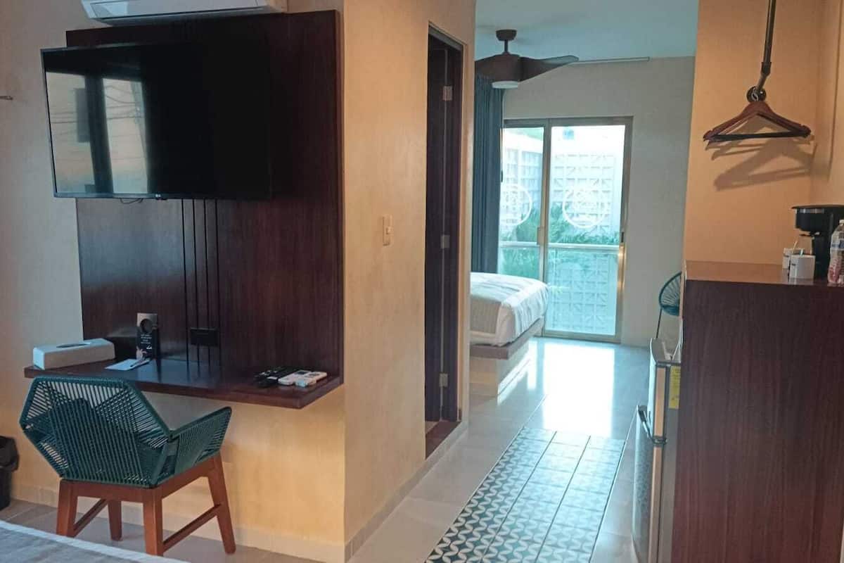 Habitación de hotel con escritorio, silla, televisión y balcón con cama.