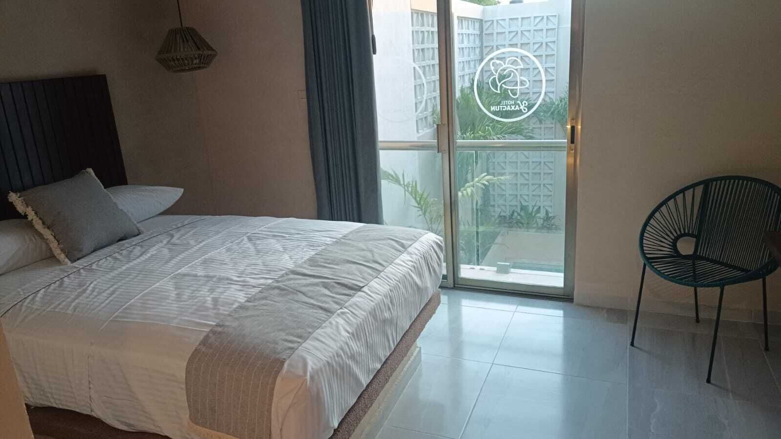 Une chambre à coucher avec un lit, une chaise et une vue sur un immeuble, visible à travers une porte vitrée.