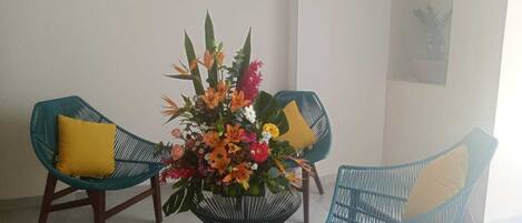 A room with two teal wicker chairs with yellow cushions, a central floral arrangement, and a tiled floor.