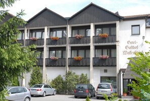 A multi-story hotel with balconies adorned with flower boxes, a parking lot with several cars, and a sign indicating the hotel's name. - Hotel-Gasthof Wasserschloß (Mitwitz)