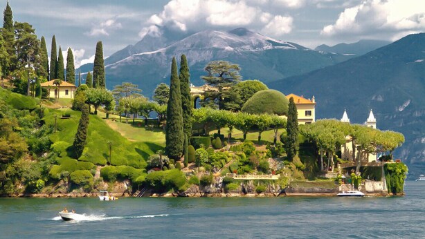Una propiedad frente al lago con jardines cuidados, montañas al fondo y un muelle.