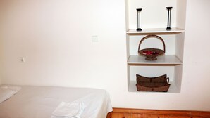 A bedroom with a single bed, a wooden headboard, a white wall, and a built-in shelf with a basket and two black floor lamps. - Mary's Villas (Lesvos)