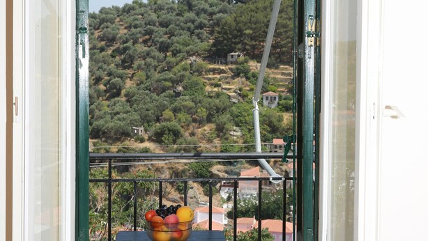 A balcony with a view of a hillside, a table with a fruit bowl, and a metal railing. - Mary's Villas (Lesvos)