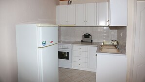 A compact kitchen with white cabinets, a built-in oven, a refrigerator, and a sink. - Mary's Villas (Lesvos)