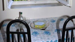 A dining table with chairs, a window with a view of a hilly landscape, and a bottle on the table. - Mary's Villas (Lesvos)