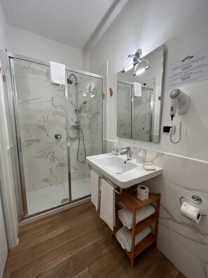 Une salle de bain moderne avec une douche à parois de verre, un lavabo blanc et un sèche-cheveux fixé au mur.
