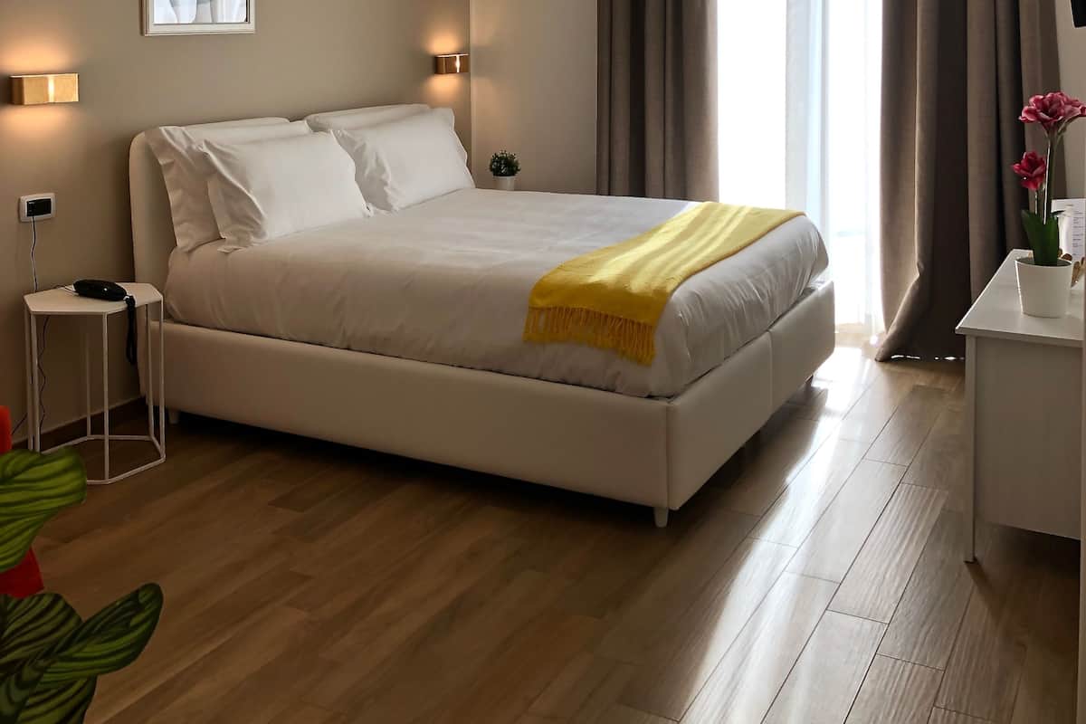 Une chambre d’hôtel avec un grand lit, des lampes de chevet, une petite table, une plante en pot et une fenêtre avec des rideaux.