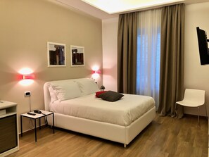 Une chambre à coucher moderne avec un lit blanc, une petite table de chevet avec un téléphone et une chaise.