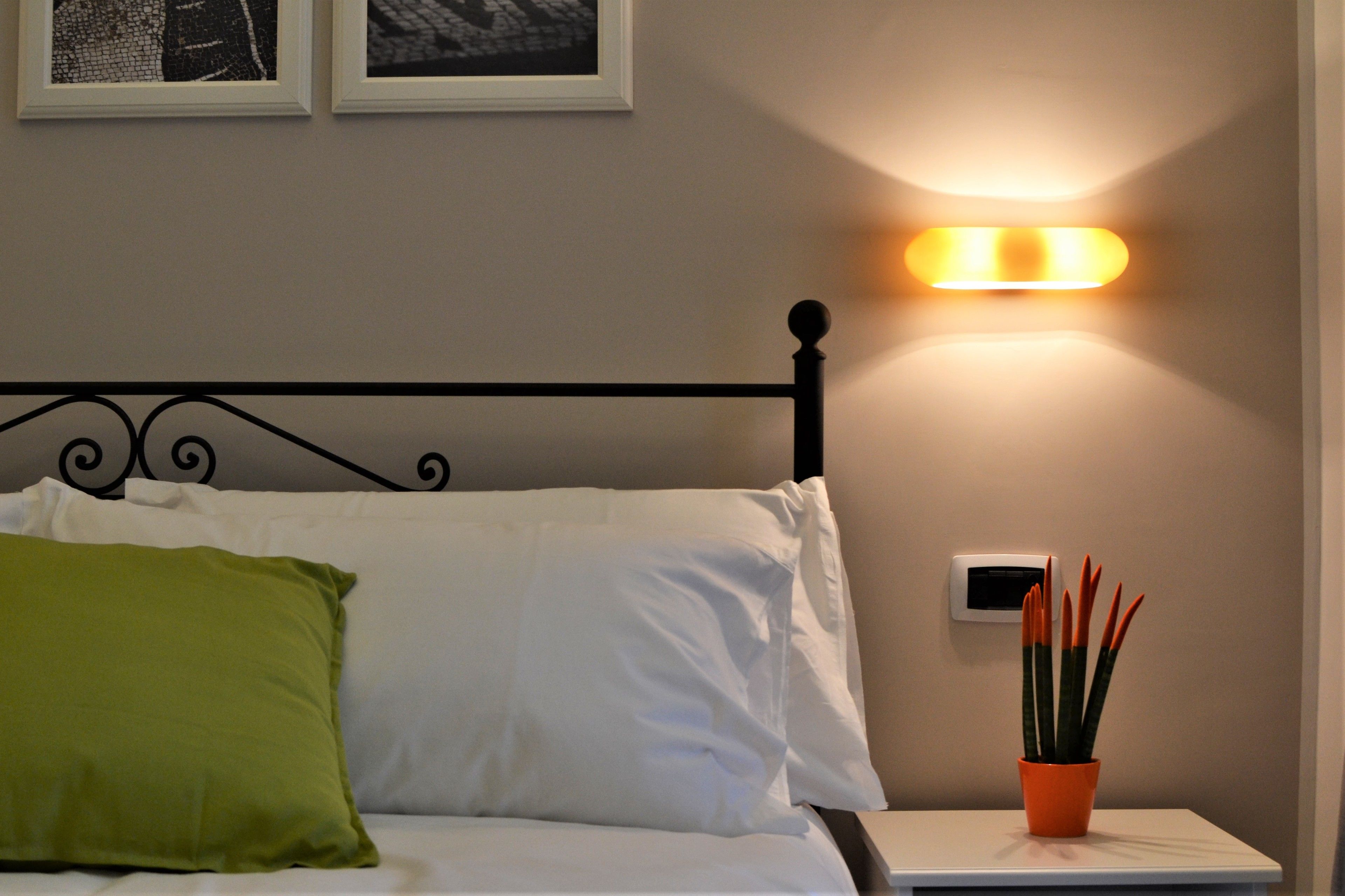 A neatly made bed with white and green pillows, a black metal headboard, and a wall-mounted light fixture.