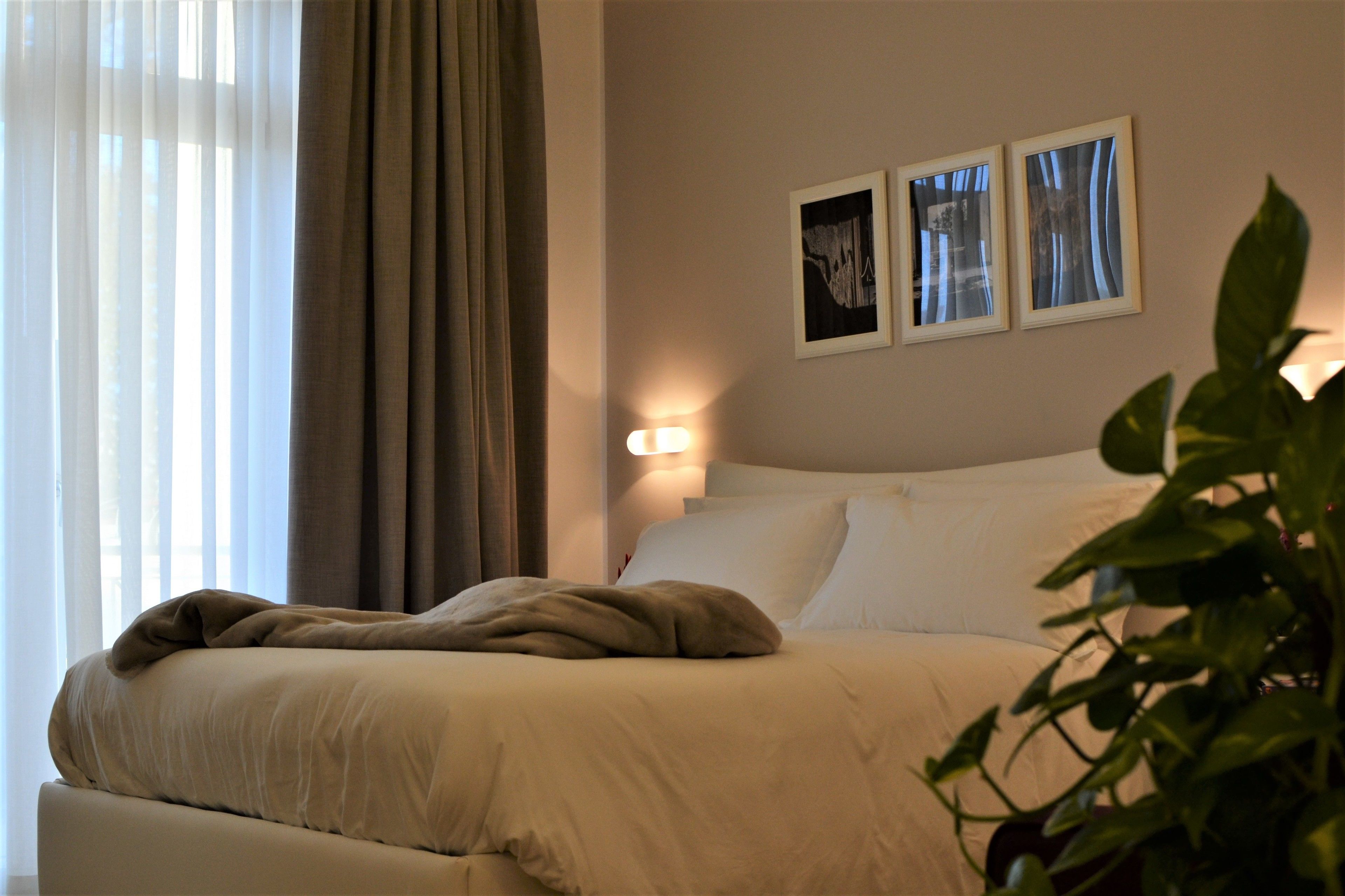 A neatly made bed with a beige blanket and pillows, a bedside lamp, and two framed pictures on the wall.