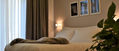 Una cama bien hecha con una manta y almohadas color beige, una lámpara de noche y dos cuadros en la pared.