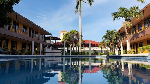 Ein Hotel mit Pool, Palmen und einem Gebäude mit rotem Dach im Hintergrund.