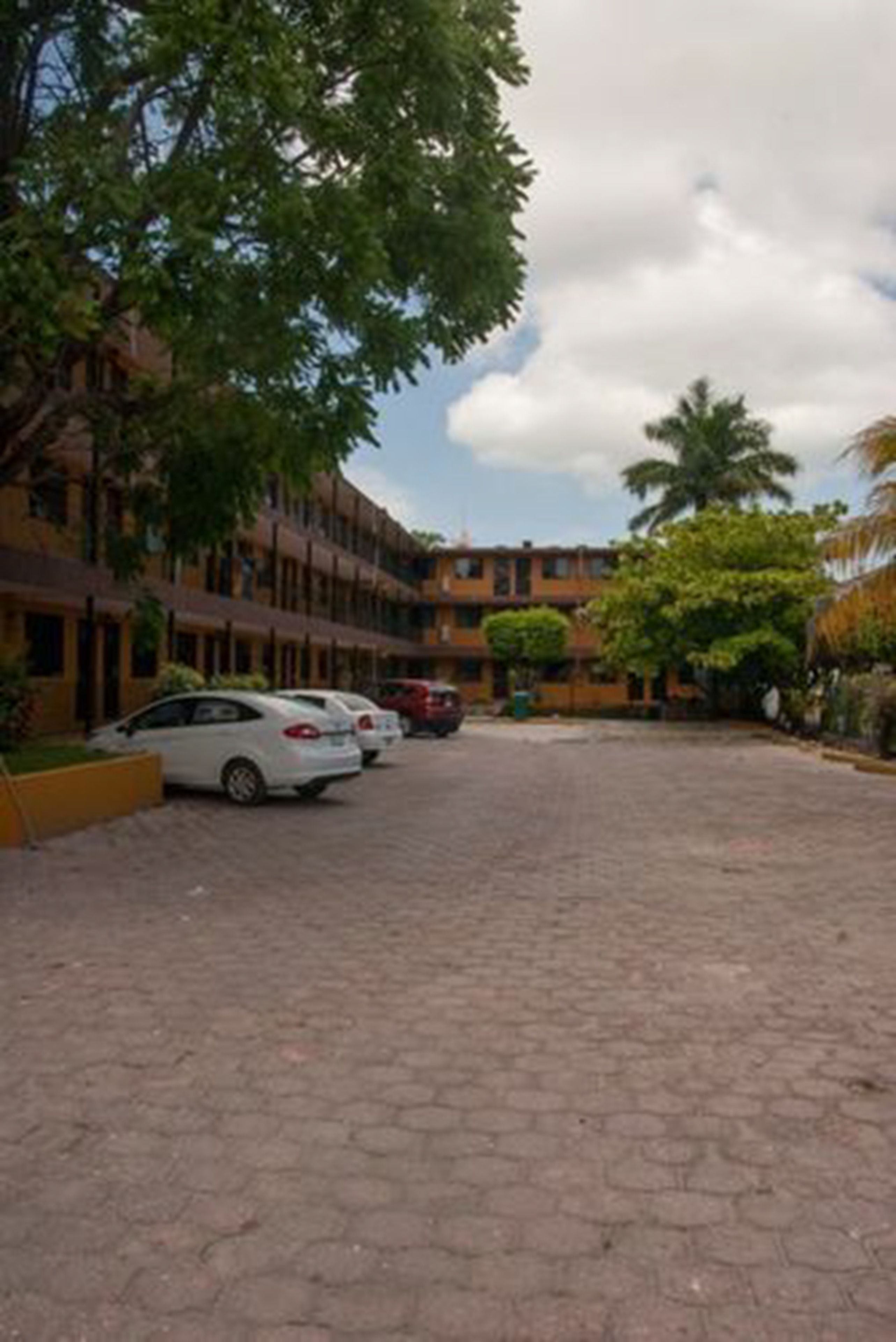 A courtyard with a paved ground, parked cars, and a building with multiple floors and balconies.
