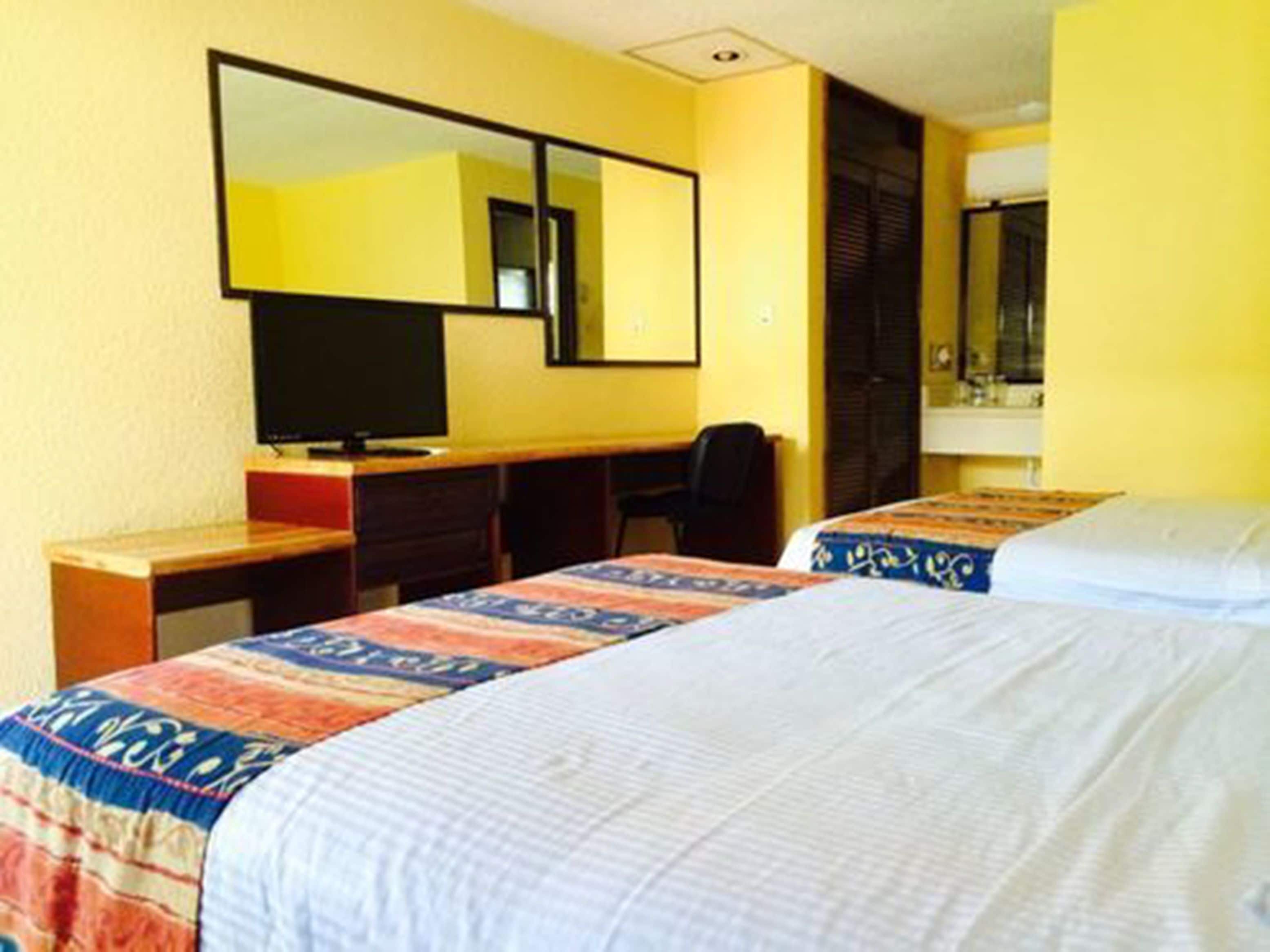 A hotel room with two beds, a desk, a chair, a television, and a mirror.