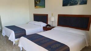 Ein Hotelzimmer mit zwei Betten, jeweils mit weißer Bettdecke und blauem, gemustertem Laufflächenteppich. Zwischen den Betten steht ein Nachttisch mit Lampe und Telefon.