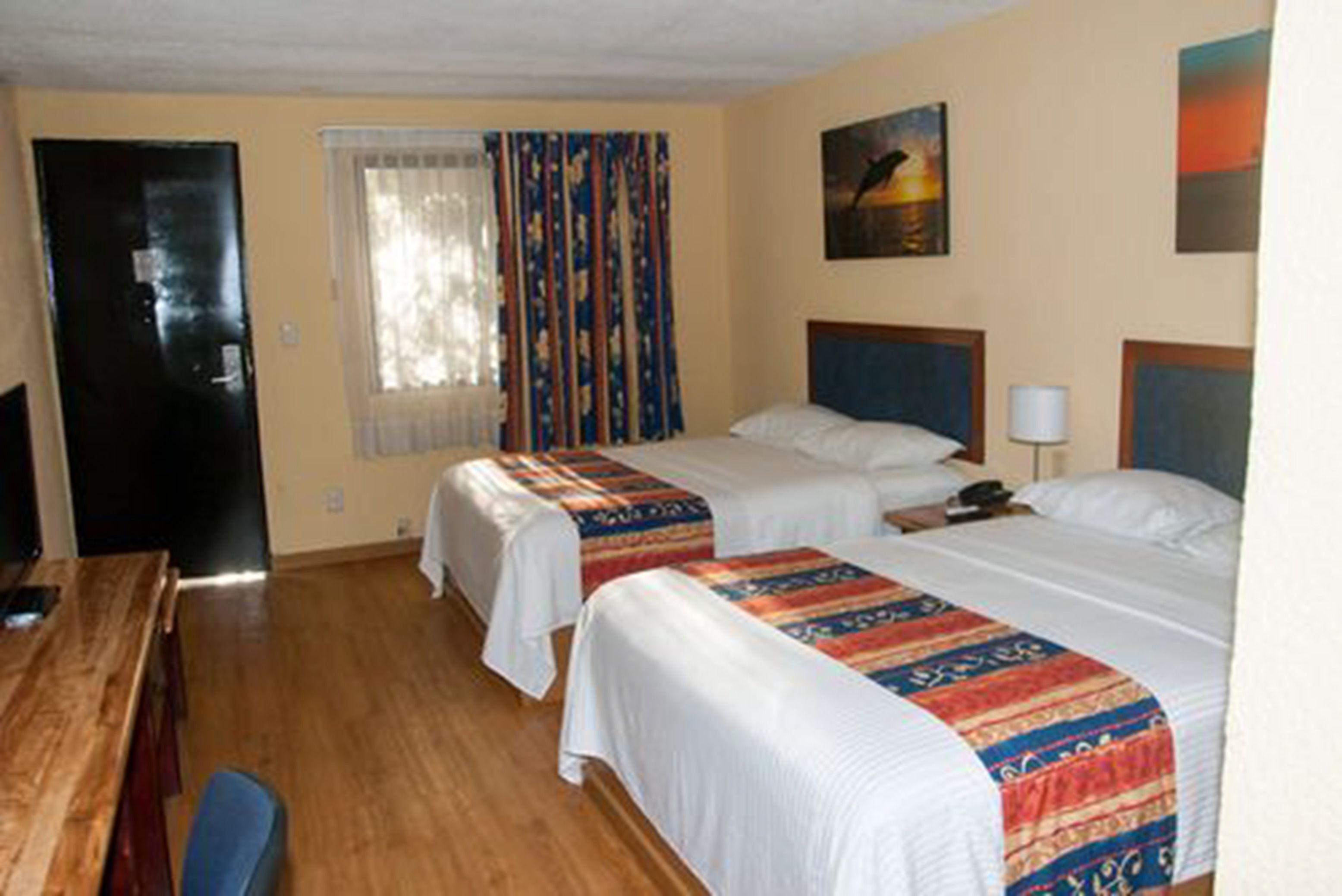Quarto de hotel com duas camas, uma escrivaninha de madeira, televisão e janela com cortinas.