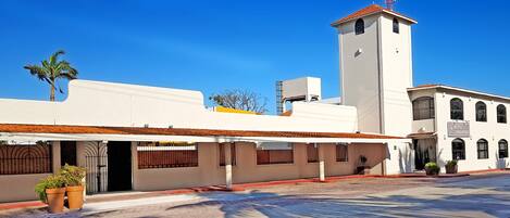 Un hotel con fachada blanca, una torre de campanas y un cartel que indica que es un hotel.