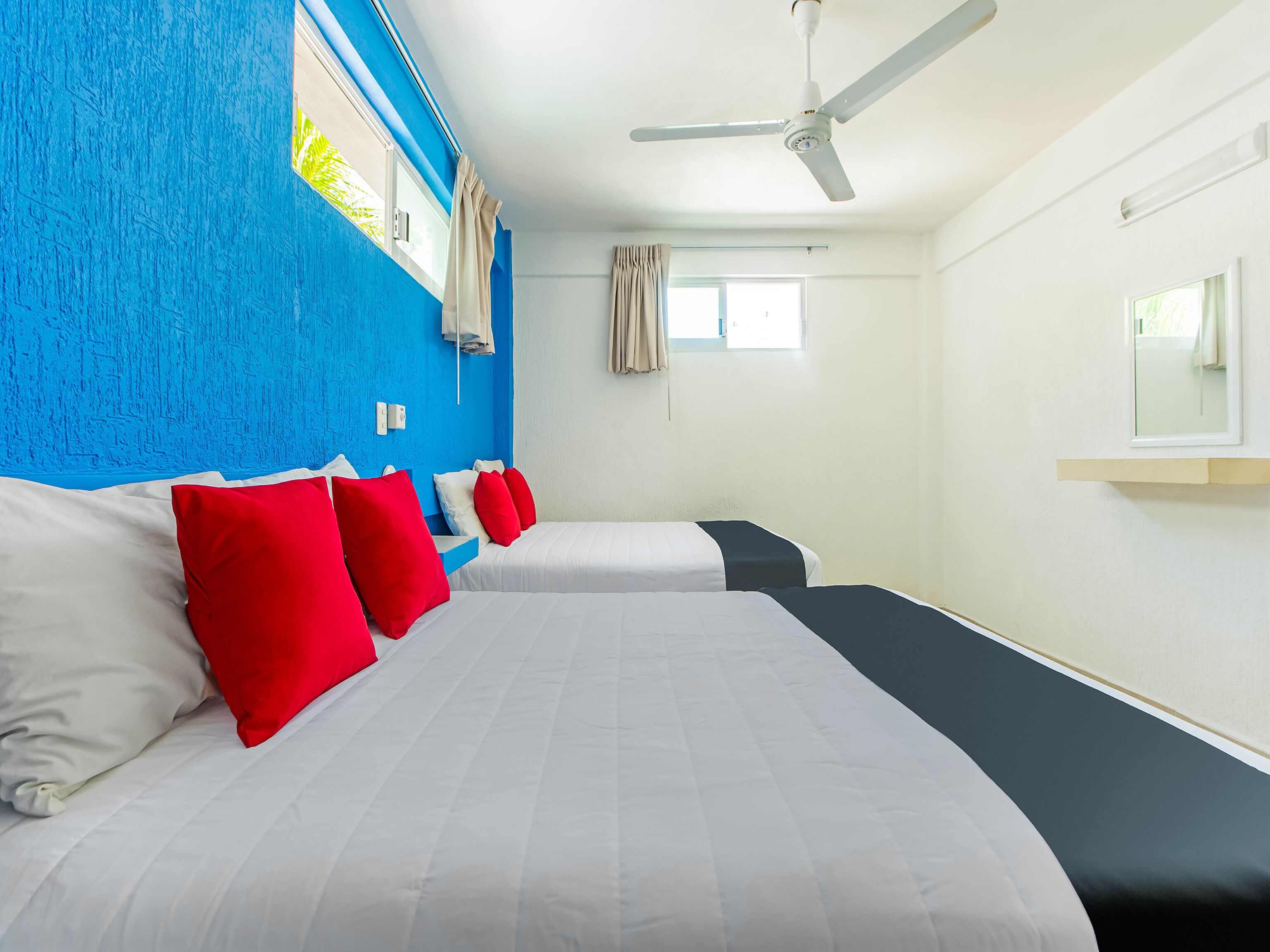 Habitación de hotel con dos camas, ventilador de techo y ventana con cortinas.