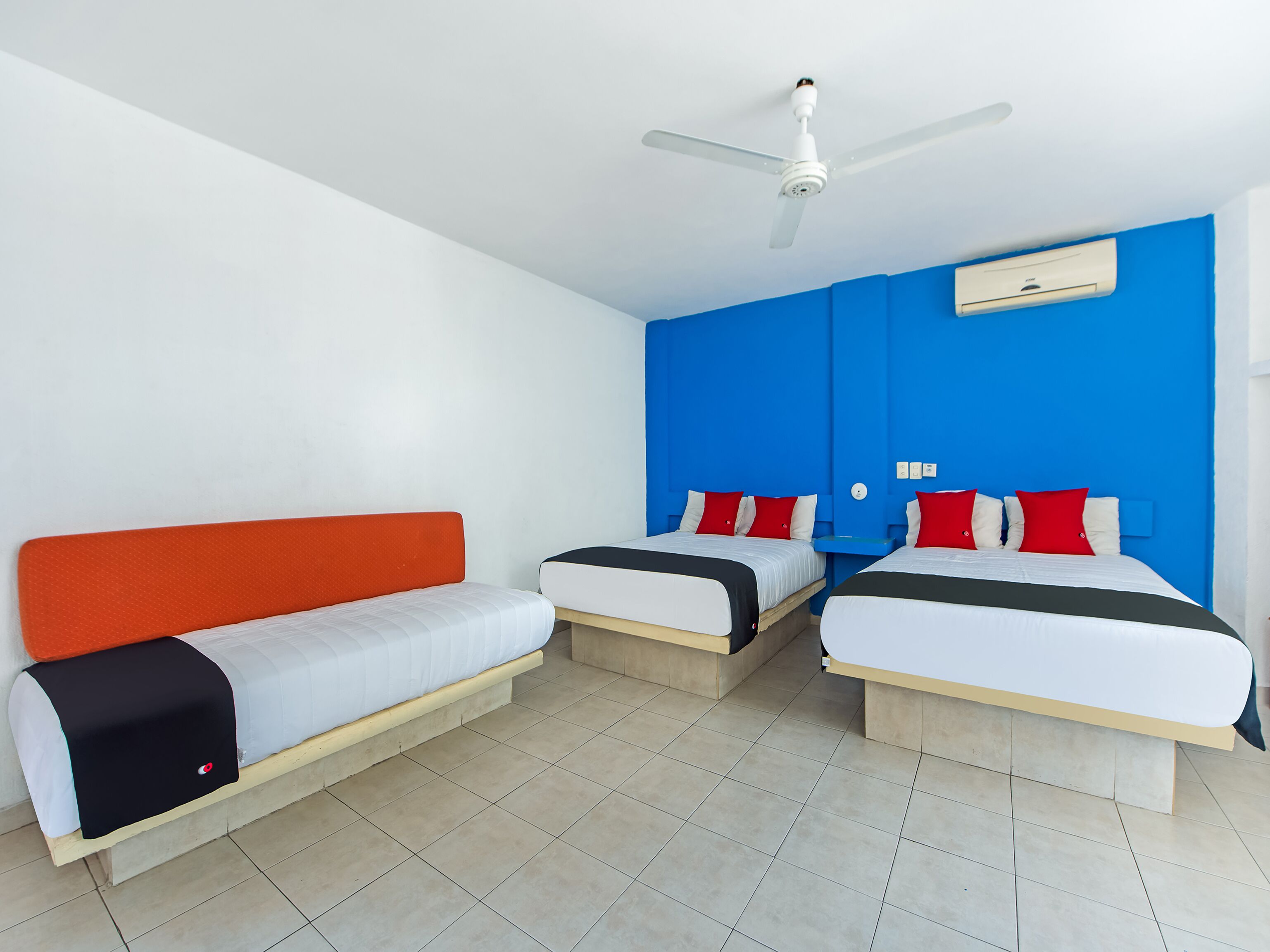 A hotel room with two single beds, a ceiling fan, and an air conditioning unit.