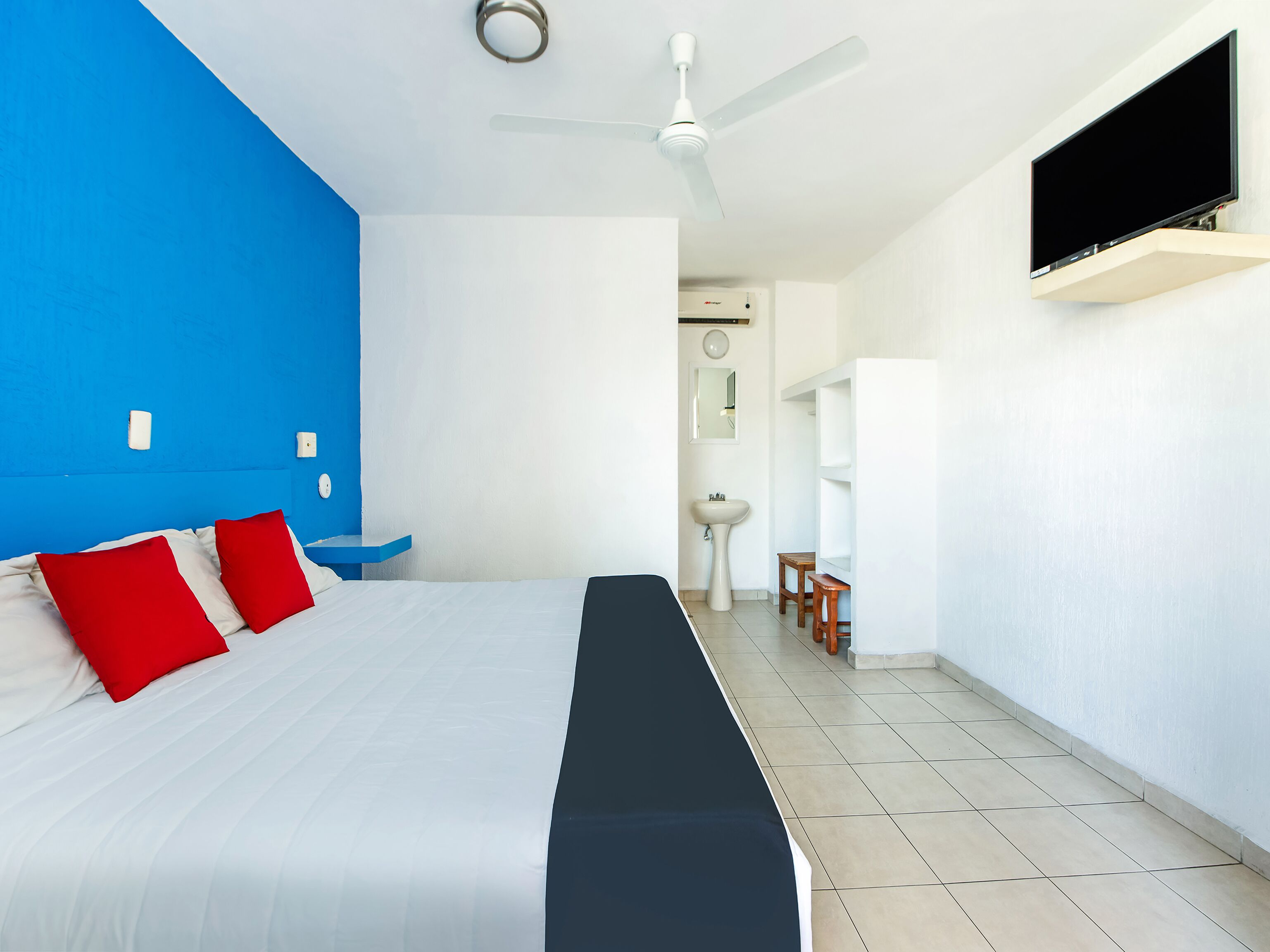 A hotel room with a large bed, a ceiling fan, a TV mounted on the wall, and a bathroom visible through an open door.
