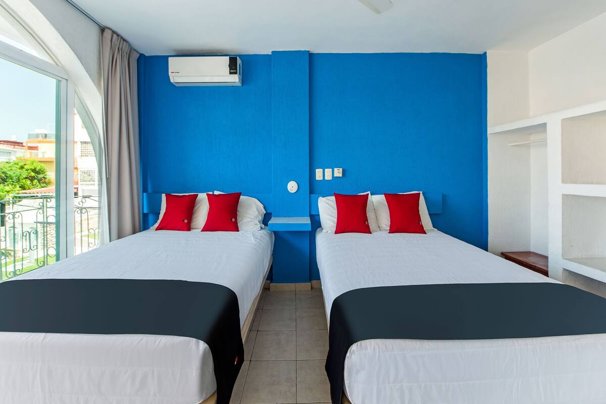 Habitación de hotel con dos camas, ventilador de techo, aire acondicionado y vista al exterior.