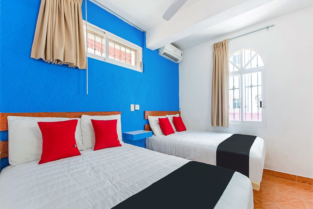 Una habitación de hotel con dos camas, paredes azules, una ventana con cortinas y un equipo de aire acondicionado.