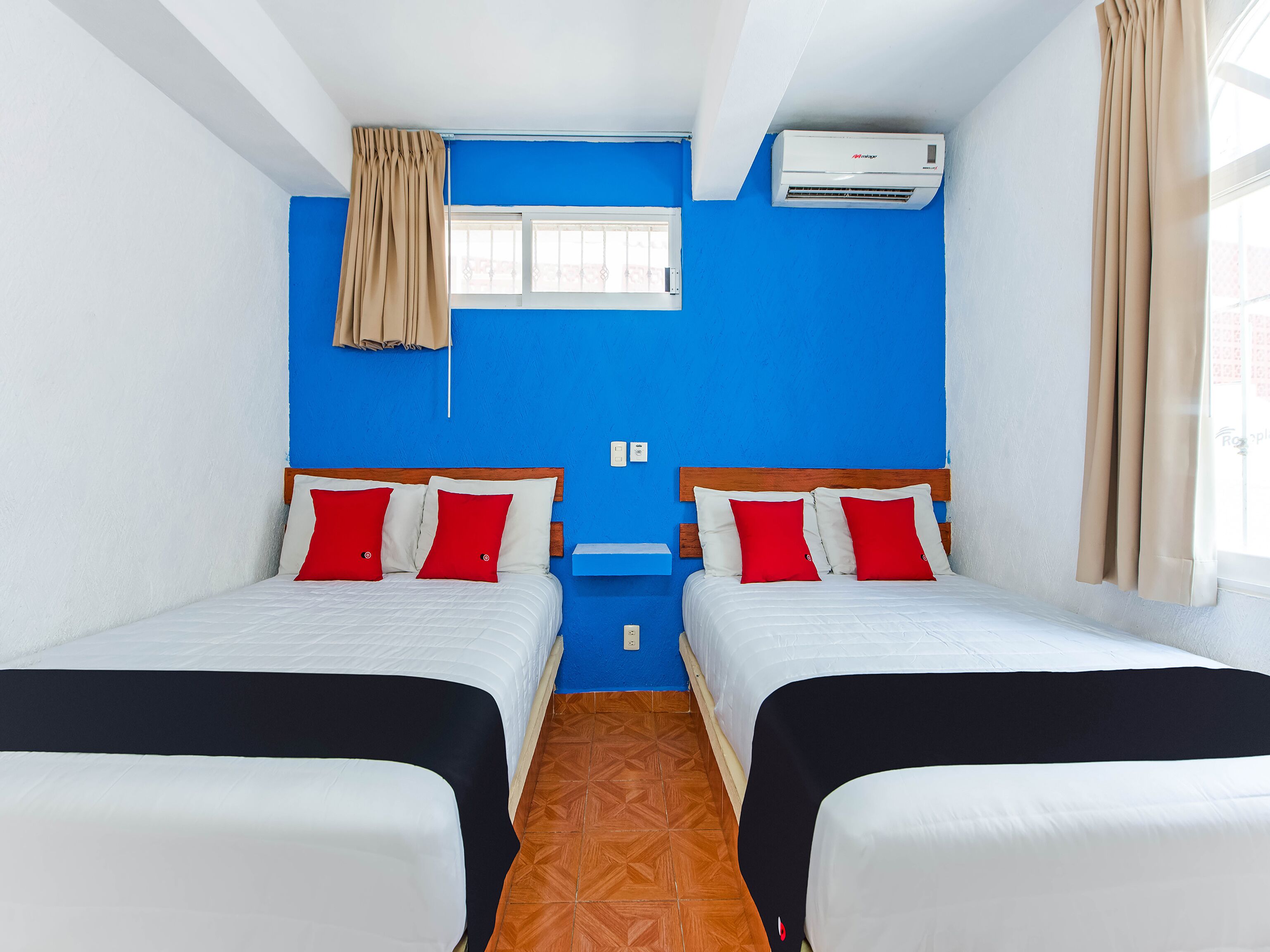 A room with two beds, a window, an air conditioner, and a blue wall.