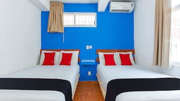 A room with two beds, a window, an air conditioner, and a blue wall.