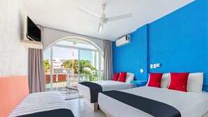 Una habitació d'hotel amb dos llits, un ventilador de sostre, aire condicionat i un balcó amb vista a la ciutat.