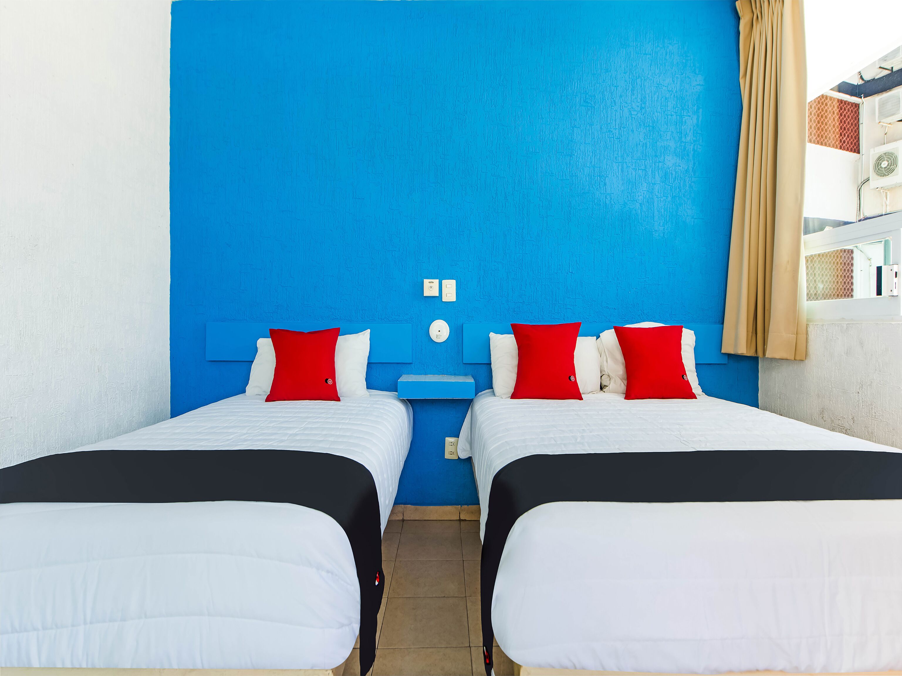 Een kamer met twee bedden, elk voorzien van witte lakens en rode kussens, tegen een blauwe muur.