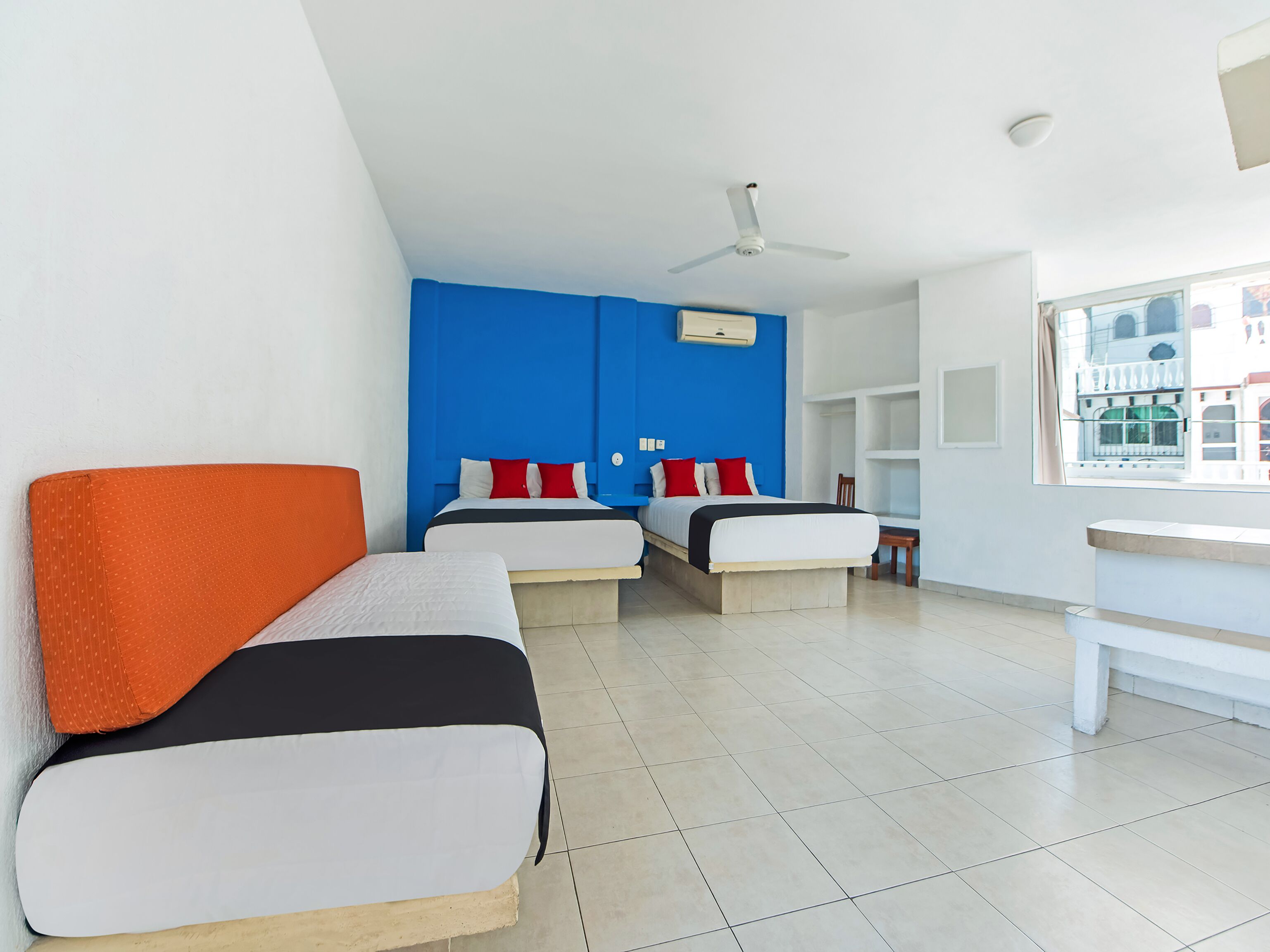 Habitación de hotel con dos camas, un ventilador de techo, una ventana con vistas y un escritorio blanco.