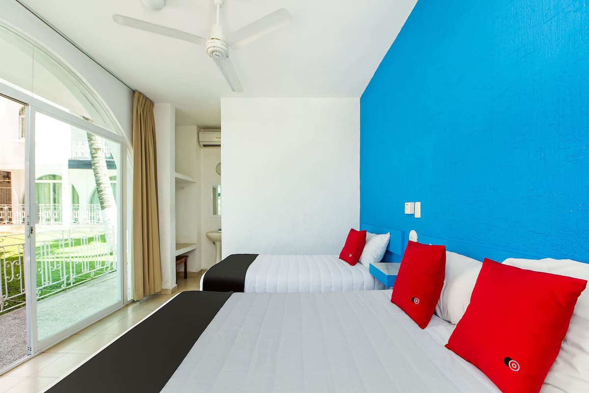 Habitación de hotel con una cama grande, ventilador de techo, baño y vistas a una piscina y un edificio.