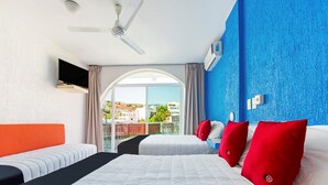 Habitació d'hotel amb un llit gran, dos llits més petits, un ventilador de sostre, una televisió i vista a la ciutat.