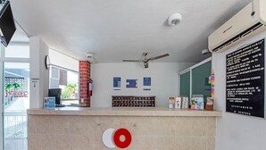 Zona de recepció d'hotel amb un taulell, un ventilador de sostre, un extintor i un panell d'anuncis amb informació.