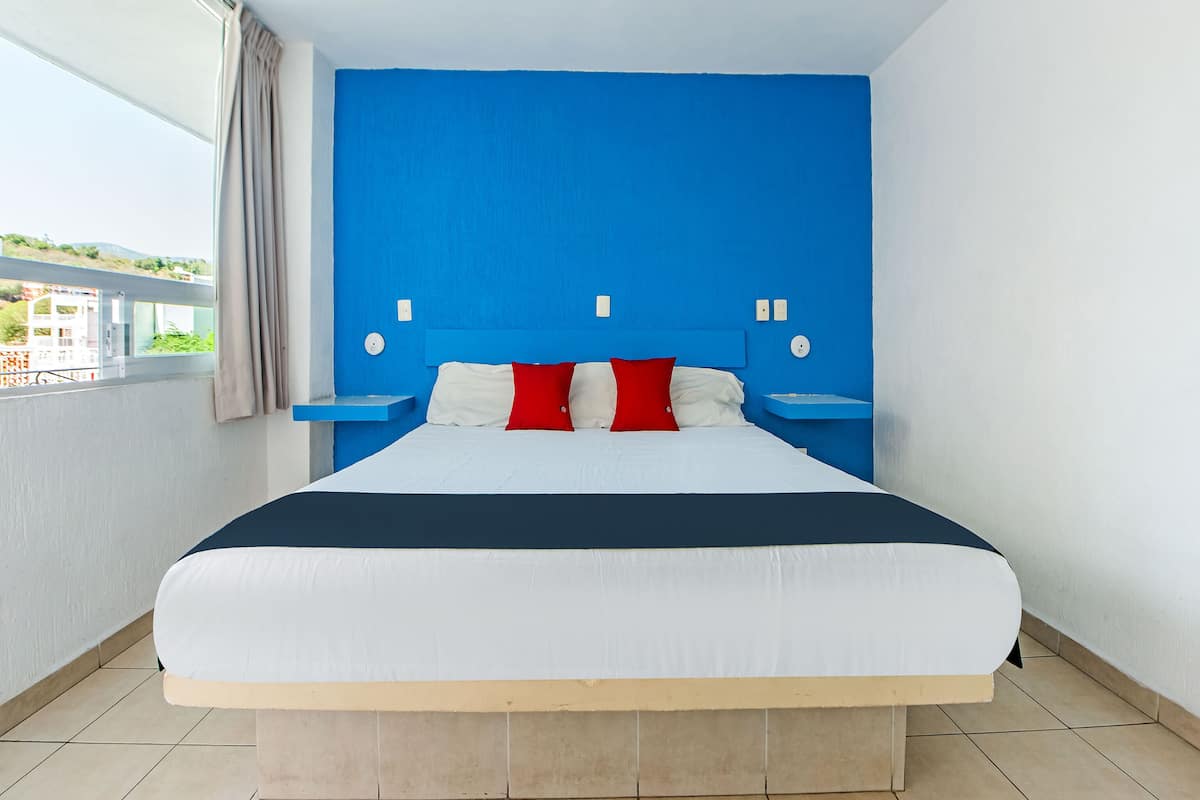 Una habitación de hotel moderna con una cama grande, paredes de acento azul y vistas a la ciudad.