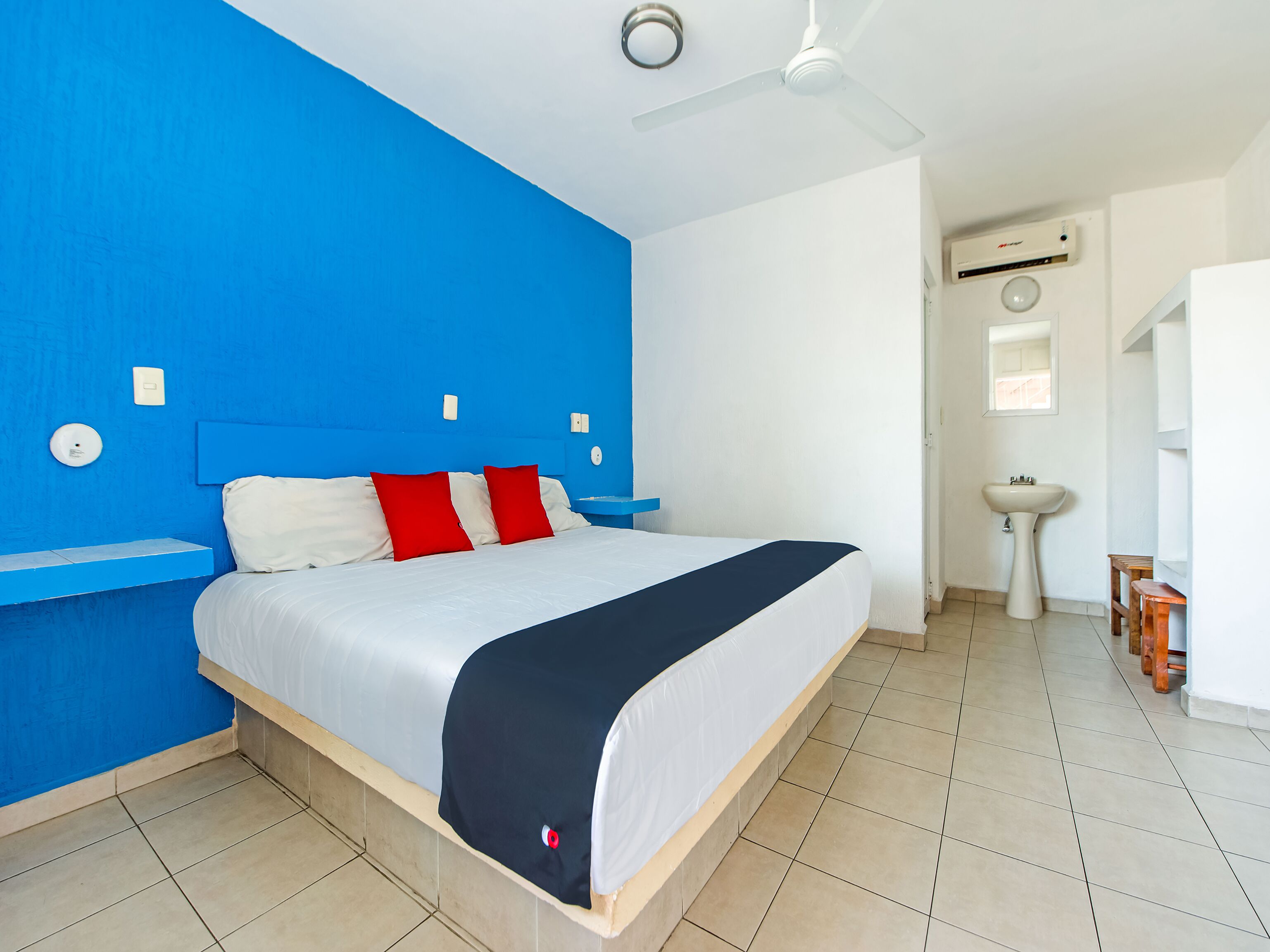 A bedroom with a bed, a ceiling fan, a white sink, and a small wooden stool.