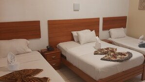 A hotel room with three single beds, wooden headboards, white linens, and a small bedside table with a phone and a tissue box. - Curuhuinsi Lodge (Iquitos)