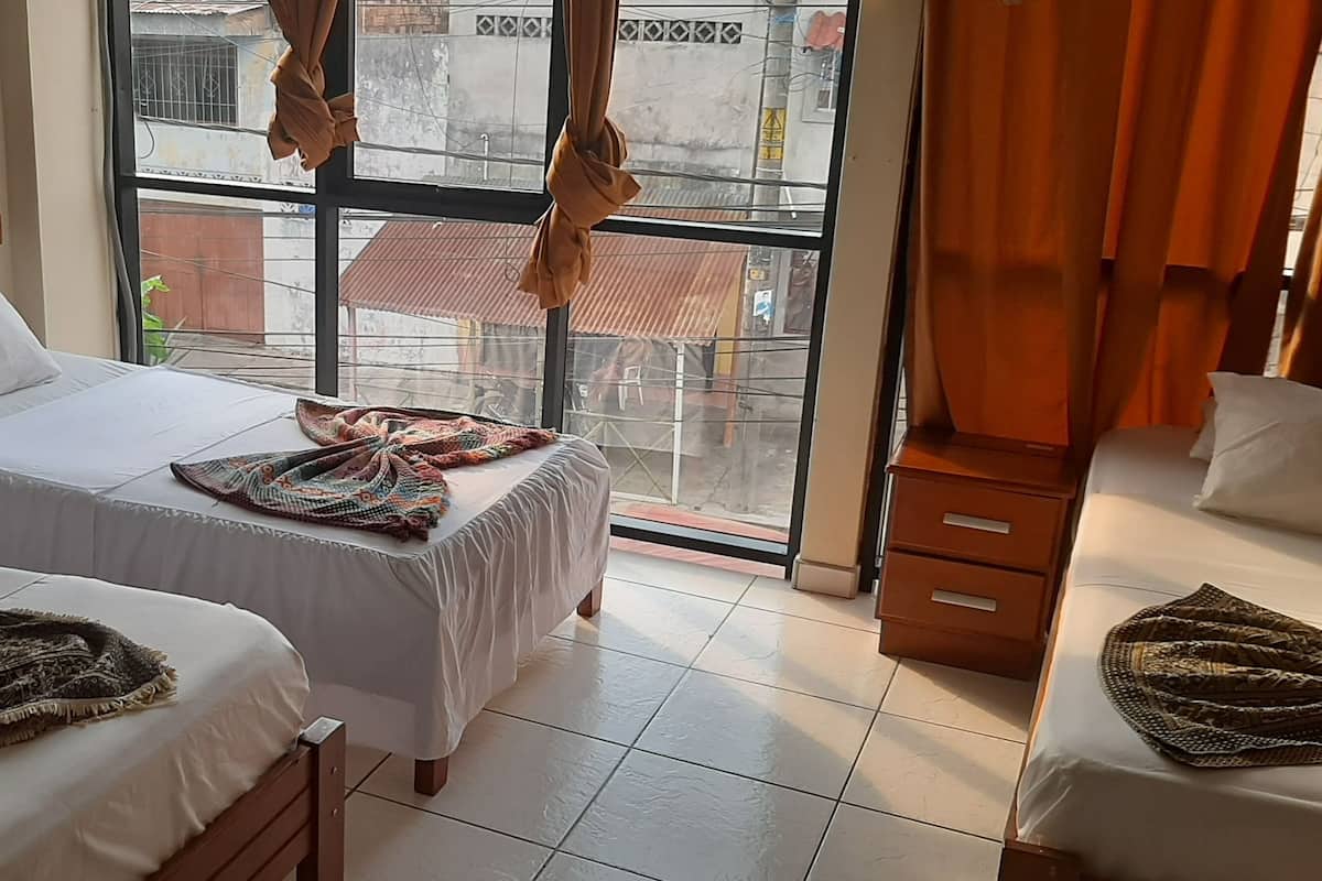 Une chambre d’hôtel avec deux lits simples, une tête de lit en bois, une grande fenêtre avec des rideaux et une vue sur l’extérieur.