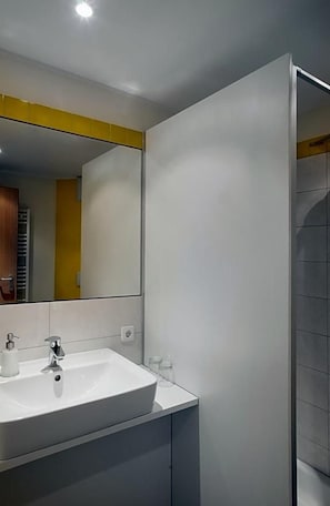 Une salle de bain moderne avec un lavabo blanc, un miroir et un mur d’accent jaune.