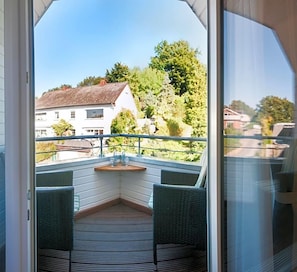 Un balcone con mobili in vimini e un pavimento in legno, con vista su una zona residenziale con case e alberi.