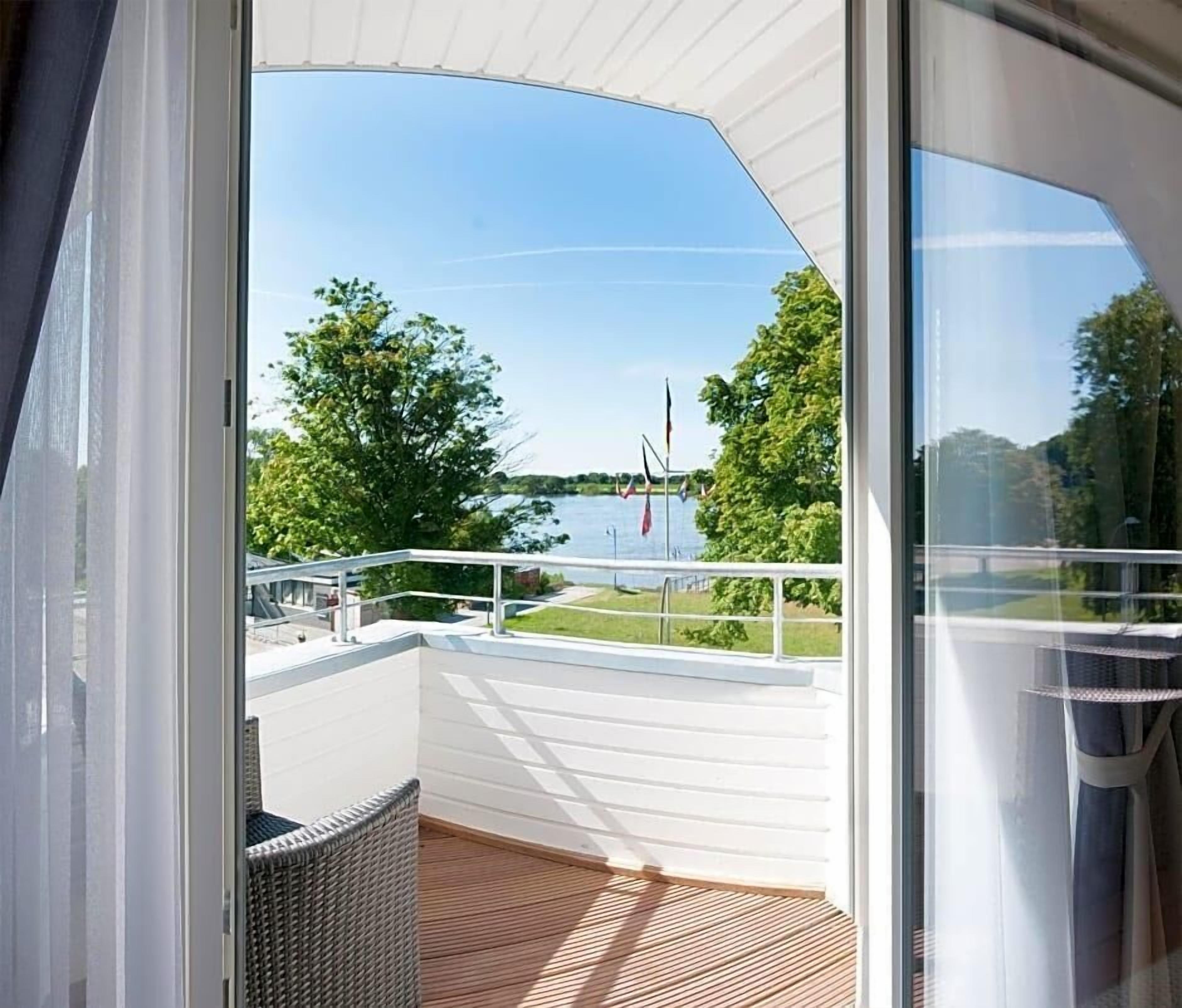 A balcony with a view of a lake, white railings, and a wicker chair.